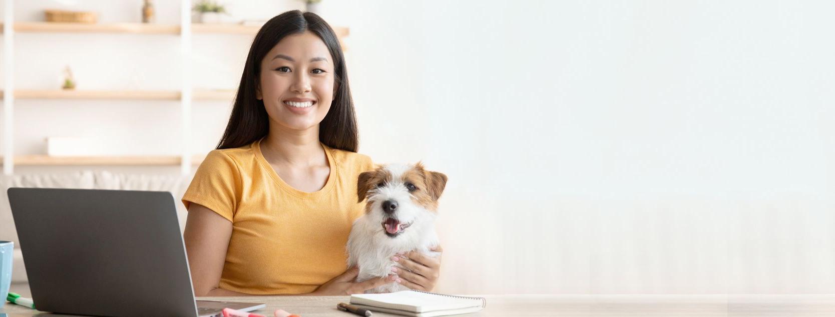 一个微笑的女人把她的狗放在她的腿上，用她的家用笔记本电脑登录Patelco在线.
